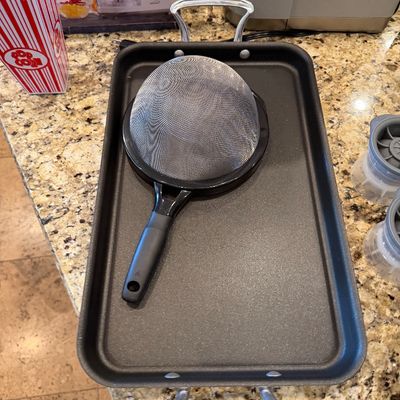Sale Photo Thumbnail #176: Rectangular nonstick double-burner griddle pan with stainless steel handles, paired with a fine mesh strainer.