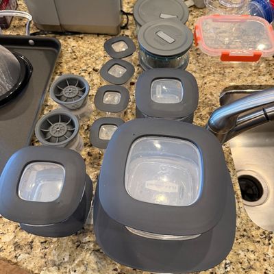 Sale Photo Thumbnail #175: Collection of Rubbermaid and Pyrex glass food storage containers with grey rubberized lids, arranged on a granite countertop alongside silicone ice sphere molds.