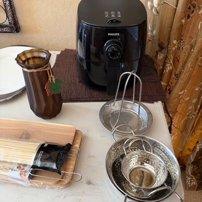 Sale Photo Thumbnail #209: Black Philips air fryer displayed alongside various kitchen accessories, including stainless steel steamer baskets, wooden cutting boards, skewers, and a decorative brown glass vase.
