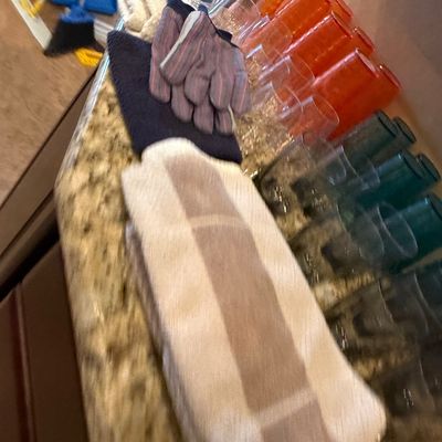 Sale Photo Thumbnail #58: Collection of assorted household items including folded towels, work gloves, and sets of colorful plastic tumblers on a granite countertop.