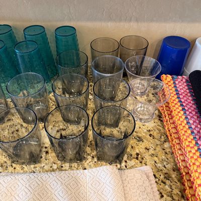 Sale Photo Thumbnail #162: Collection of modern plastic and glass drinking tumblers, including smoked grey, teal ribbed, and clear styles, arranged on a kitchen countertop alongside colorful placemats.
