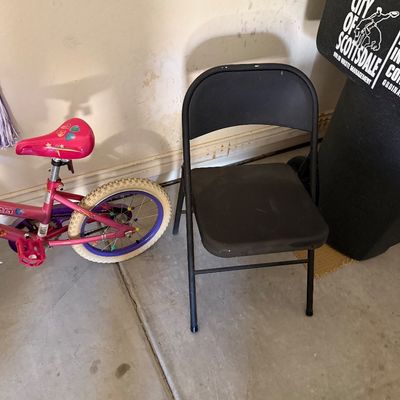 Sale Photo Thumbnail #106: Black metal folding chair with plastic seat and back, standing next to a pink children's bicycle in a garage.