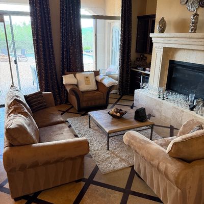 Sale Photo Thumbnail #46: Contemporary living room furniture set including a tan suede sofa, two matching armchairs, and a metal-framed wood coffee table, anchored around a stone fireplace.