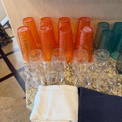Sale Photo Thumbnail #158: Collection of plastic and glass drinkware including tall orange and blue textured tumblers and stemless clear glasses, arranged on a granite countertop.