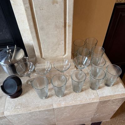 Sale Photo Thumbnail #41: Collection of ribbed clear glassware, including highball glasses and martini stems, paired with a stainless steel ice bucket and wooden coaster set.