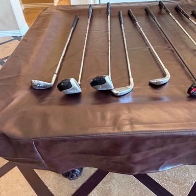 Sale Photo Thumbnail #254: Assorted golf clubs, including irons and fairway woods, laid out on a pool table cover.