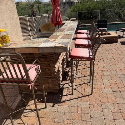 Sale Photo Thumbnail #248: Set of metal patio bar stools with pink cushions lining a tiled outdoor island bar, featuring a red umbrella.