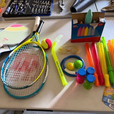 Sale Photo Thumbnail #88: Collection of sports and outdoor recreation items, including tennis racquets, pickleball paddles, sidewalk chalk, swim goggles, and bubble wands.