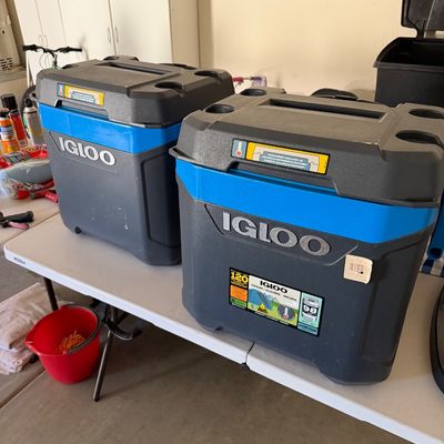 Sale Photo Thumbnail #102: Two large modern Igloo coolers in blue and grey, sitting on a folding white table.
