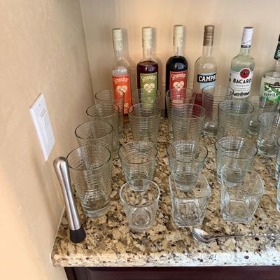Sale Photo Thumbnail #42: Collection of modern ribbed glassware, bar tools, and assorted liquor bottles displayed on a granite countertop bar area.