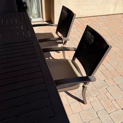 Sale Photo Thumbnail #247: Modern outdoor dining dining set featuring a slatted dark brown metal table and matching woven-back armchairs with neutral seat cushions.