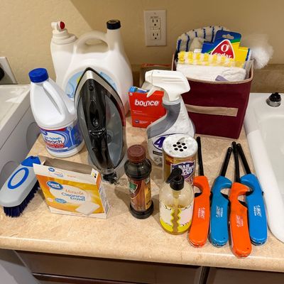 Sale Photo Thumbnail #116: Assorted household cleaning supplies, laundry detergent, clothes iron, and utility lighters set on a laundry room countertop.