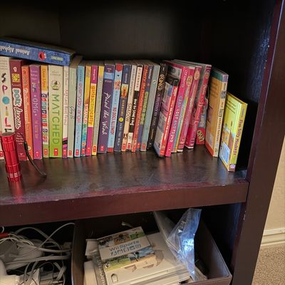 Sale Photo Thumbnail #69: Dark wood bookshelf filled with children's chapter books, DVDs, and a storage bin containing a Wii Sports game disc with associated cords and accessories.