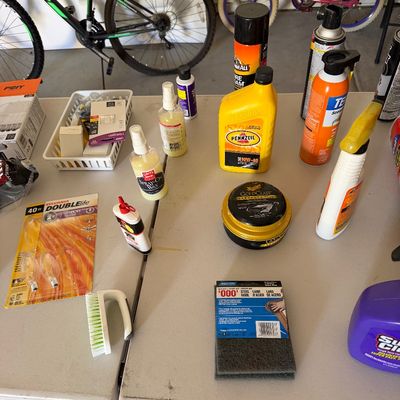 Sale Photo Thumbnail #97: Assortment of garage items including automotive fluids, detailing waxes, cleaning supplies, light bulbs, and steel wool arranged on a folding table.