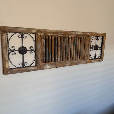 Sale Photo Thumbnail #110: Rustic wall-hanging panel featuring a distressed wood frame, central slatted wood section, and wrought iron scrollwork inserts on either side.