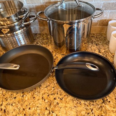 Sale Photo Thumbnail #179: Assorted modern cookware set including a stainless steel stockpot with a glass lid, nested steaming pots, and two non-stick frying pans.