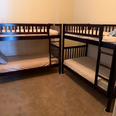 Sale Photo Thumbnail #70: Two dark stain wooden bunk bed frames, each fitted with mattresses and integrated ladders.