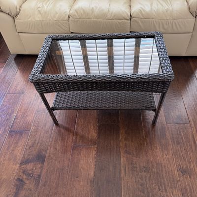 Sale Photo Thumbnail #13: Dark brown woven resin wicker coffee table featuring a glass insert top and a lower display shelf, positioned in front of a cream leather sofa.