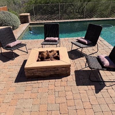 Sale Photo Thumbnail #235: Set of four modern dark brown woven resin lounge chairs with metal frames and purple accent pillows, arranged around an outdoor fire pit by a pool.