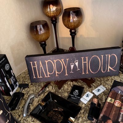 Sale Photo Thumbnail #50: Barware and cigar accessories set including a black and copper 'Happy Hour' wooden sign, amber crackle glass pedestal candle holders, a Club Macanudo ashtray, wine openers, and lighters.