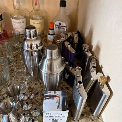 Sale Photo Thumbnail #36: Barware collection including stainless steel cocktail shakers, stainless hip flasks, small funnels, jiggers, shot glasses, and liquor bottles.
