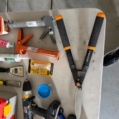 Sale Photo Thumbnail #76: Assortment of household and garden tools including Fiskars loppers, caulk guns with adhesive tubes, putties, putty knives, and a cordless power drill.