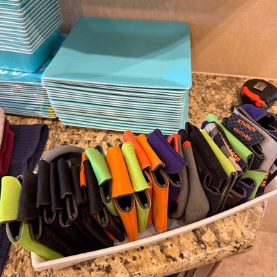 Sale Photo Thumbnail #166: Large collection of colorful foam and neoprene can koozies arranged in a white tray next to stacks of turquoise melamine plates and bowls.