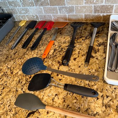 Sale Photo Thumbnail #177: Assorted modern kitchen utensils, including silicone spatulas, turners, a slotted skimmer, and a basting brush, arranged on a granite countertop.