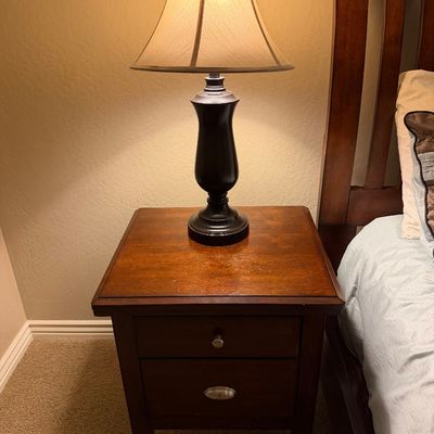 Sale Photo Thumbnail #135: Traditional dark wood nightstand featuring a single top drawer with silver hardware and a dark metal urn-style table lamp with a beige fabric shade.