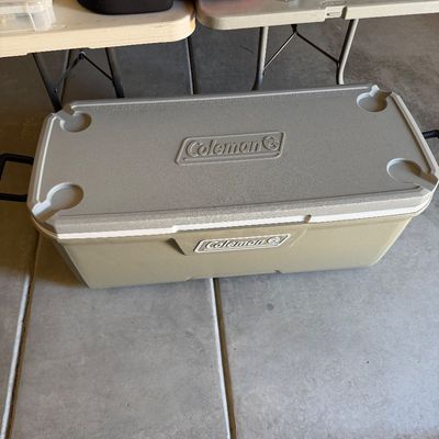 Sale Photo Thumbnail #93: Large tan Coleman ice chest cooler sitting on a garage floor, appearing in good condition.