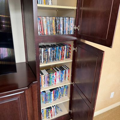 Sale Photo Thumbnail #220: Large collection of DVDs and Blu-rays organized inside a dark wood entertainment center cabinet.