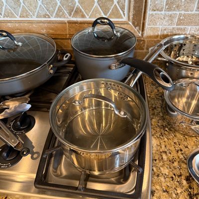Sale Photo Thumbnail #178: Assorted cookware collection including stainless steel and non-stick pots, pans, and glass lids arranged on a stovetop and countertop.