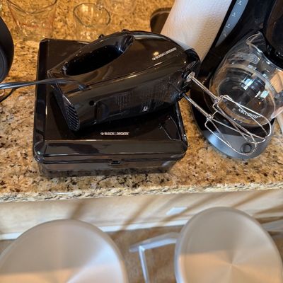 Sale Photo Thumbnail #203: Black & Decker hand mixer with beaters resting on its storage case, positioned on a kitchen counter.