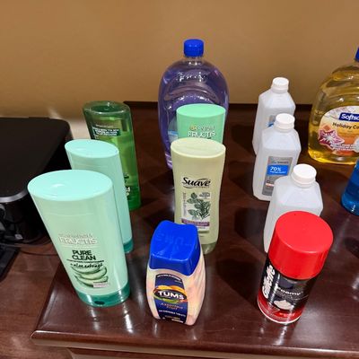 Sale Photo Thumbnail #149: Assortment of personal care products and toiletries including Garnier Fructis shampoo and conditioner, Suave shampoo, Tums, Gillette shaving cream, and isopropyl alcohol on a wooden table.