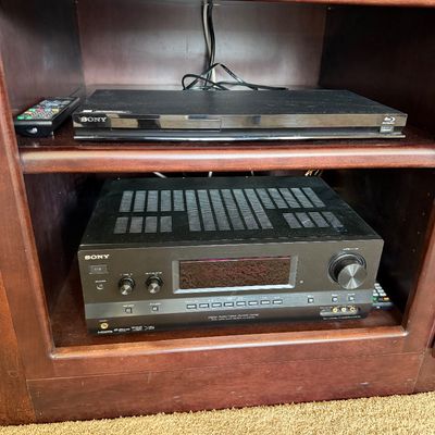 Sale Photo Thumbnail #218: Sony AV receiver and slim Sony Blu-ray player with remote control, housed inside a dark wood entertainment cabinet.