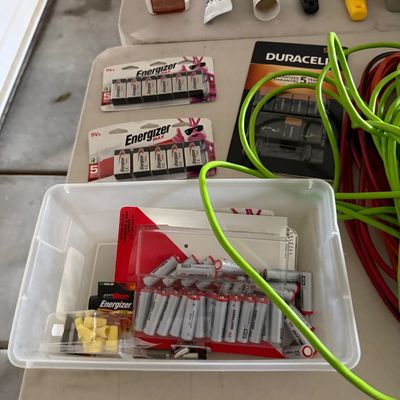 Sale Photo Thumbnail #84: Assortment of household items including Energizer 9V batteries, Kirkland Signature AA batteries in a plastic tub, extension cords, wood filler, caulk, and putty knives.