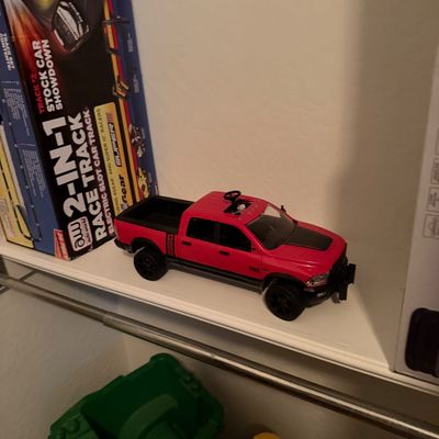 Sale Photo Thumbnail #63: Red and black toy Ram pickup truck displayed alongside boxed slot car race track sets.