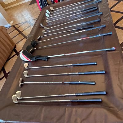 Sale Photo Thumbnail #260: Large collection of assorted golf clubs laid out on a pool table, featuring drivers, irons, and putters, with golf bags visible in the background.