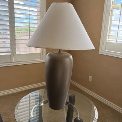 Sale Photo Thumbnail #239: Contemporary taupe ceramic table lamp with a flared white fabric shade, sitting on a round glass-top side table.