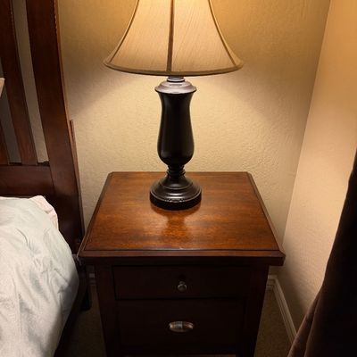 Sale Photo Thumbnail #129: Traditional dark wood nightstand with drawers topped with a dark urn-style table lamp.