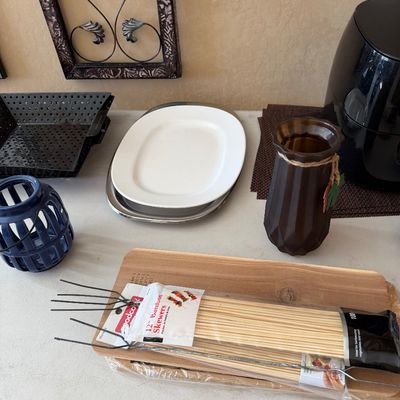 Sale Photo Thumbnail #212: Collection of kitchenware and decor including bamboo skewers, wire roasting forks, a wooden cutting board, serving platters, decorative vases, and a black air fryer.