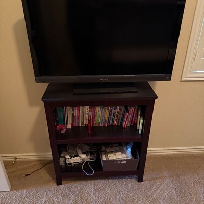 Sale Photo Thumbnail #65: Sony Bravia flat-screen television resting on a dark wood media shelf filled with books and gaming accessories.