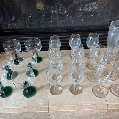 Sale Photo Thumbnail #43: Large collection of assorted glassware, featuring green-stemmed margarita glasses and clear wine glasses arranged on a stone surface.