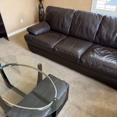 Sale Photo Thumbnail #227: Contemporary dark brown leather three-cushion sofa featuring white contrast stitching, shown alongside a modern oval glass-top coffee table.