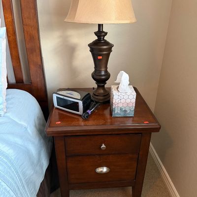 Sale Photo Thumbnail #119: Traditional dark wood nightstand with two drawers, featuring a bronze-finish table lamp and a digital alarm clock.