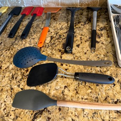 Sale Photo Thumbnail #163: Assorted modern kitchen utensils including silicone spatulas, spatulas, and skimmers laid out on a granite countertop.