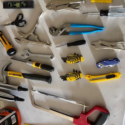 Sale Photo Thumbnail #75: Assortment of hand tools including locking pliers, a Stanley hammer, a hacksaw, Channellock pliers, Hex key sets, and utility knives arranged on a white table.