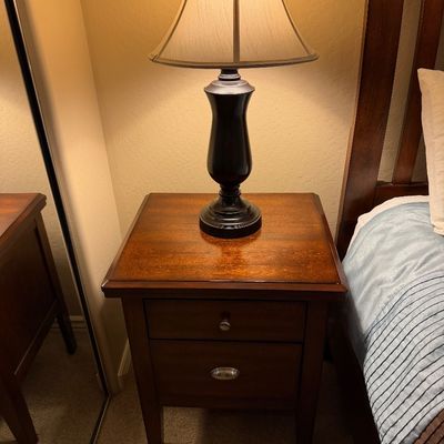 Sale Photo Thumbnail #131: Traditional dark wood two-drawer nightstand with a dark bronze table lamp topped by a bell lampshade.