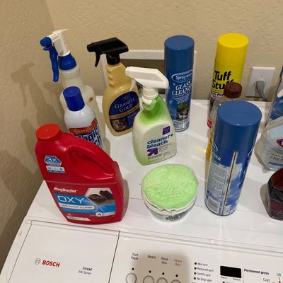 Sale Photo Thumbnail #105: Assorted household cleaning supplies, including Rug Doctor OXY cleaner, Sprayway glass cleaner, Granite Gold, and Tuff Stuff spray, displayed atop a white Bosch Nexxt washing machine.