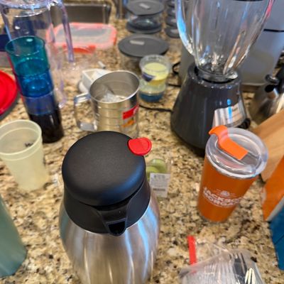 Sale Photo Thumbnail #165: Assorted kitchenware including a stainless steel thermal carafe, a glass blender with a grey base, a travel mug, plastic cups, and various storage containers on a granite countertop.